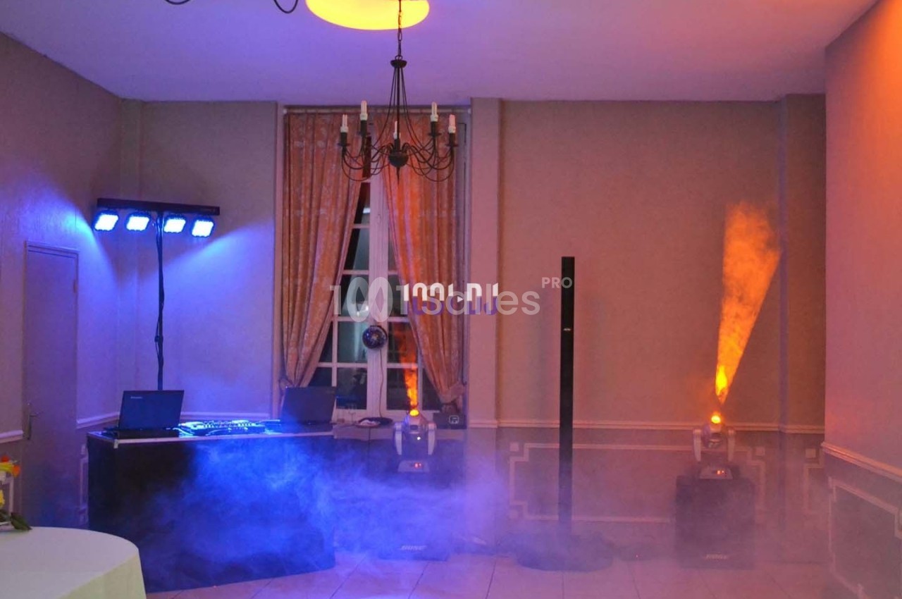 Salle équipée pour un événement avec jeux de lumière, table de mixage et fumée diffusée au sol.