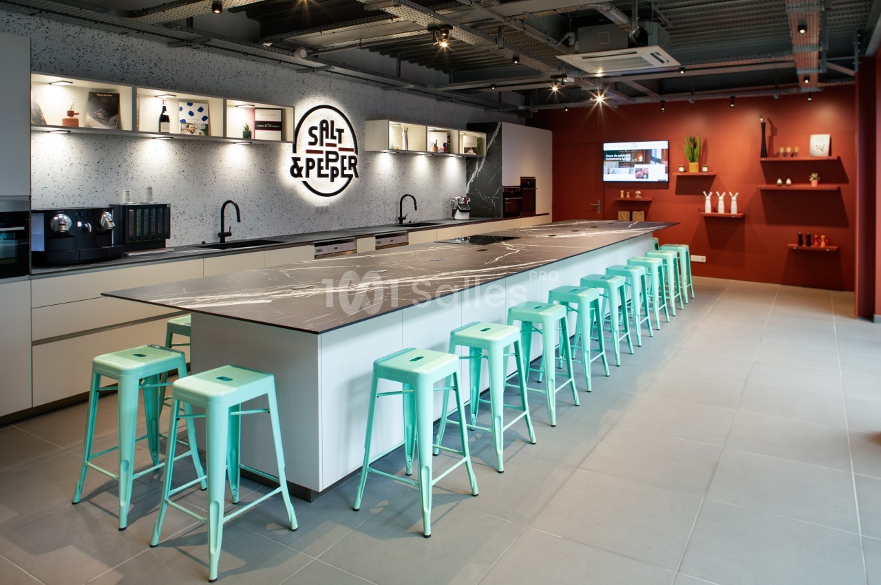 Cuisine moderne avec un long îlot central, tabourets turquoise, étagères décoratives et éclairage intégré.