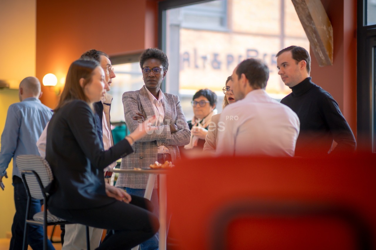 Un groupe de personnes discute debout autour d'une table haute dans un espace intérieur lumineux.