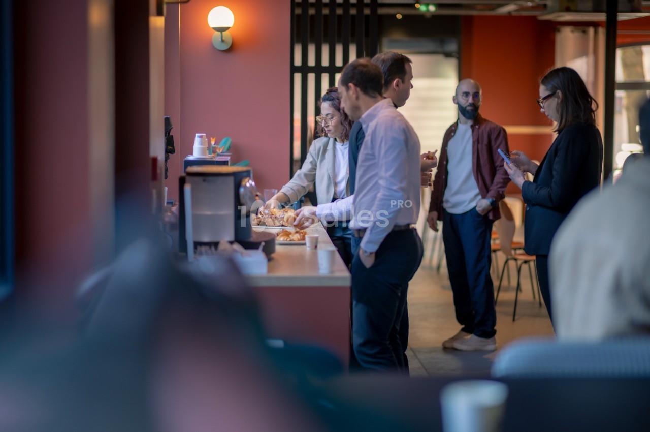 Des personnes discutent et se servent des viennoiseries près d'une machine à café dans un espace convivial.