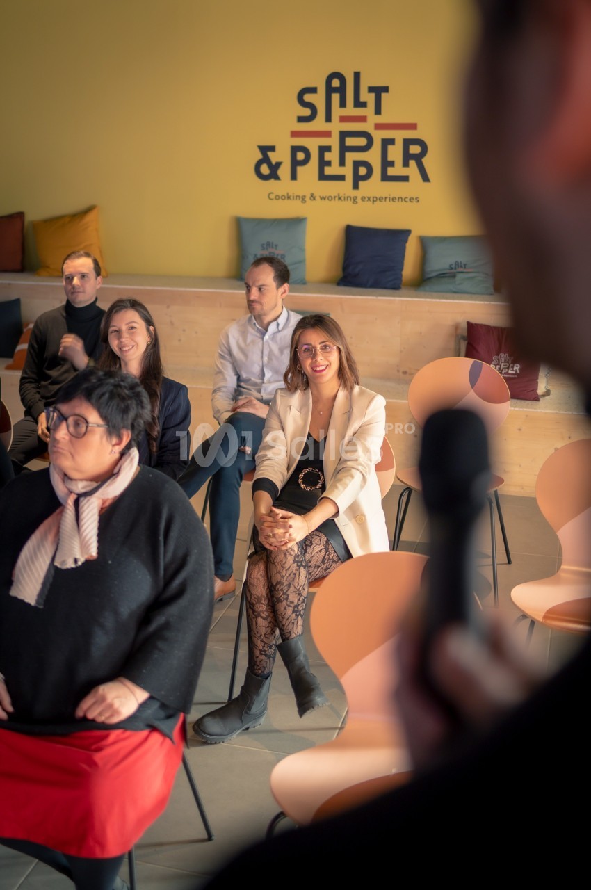 Personnes assises dans une salle lors d'une présentation, avec un intervenant tenant un micro au premier plan.