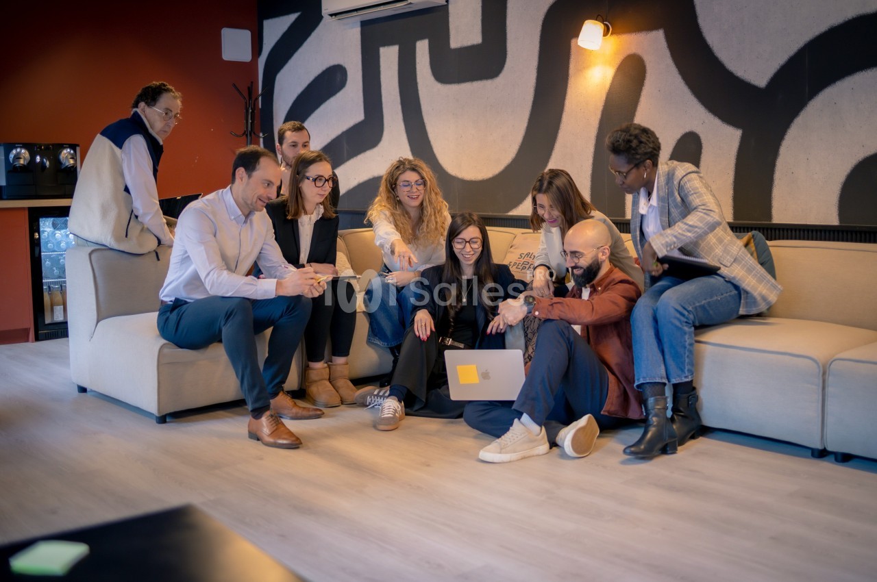 Un groupe de personnes assises sur un canapé et au sol, échangeant autour d'un ordinateur portable dans un espace moderne.