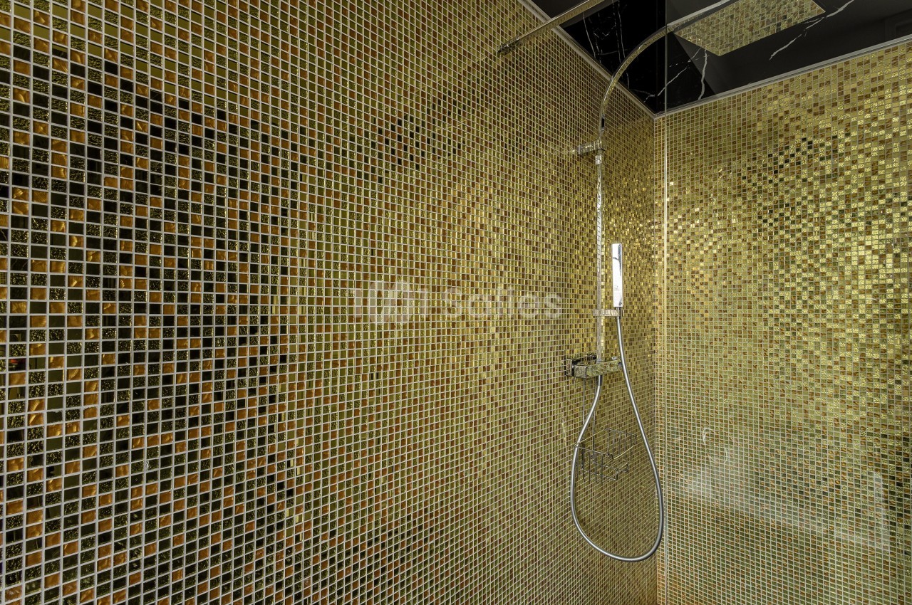 Douche moderne avec carrelage en mosaïque dorée et pommeau de douche mural.