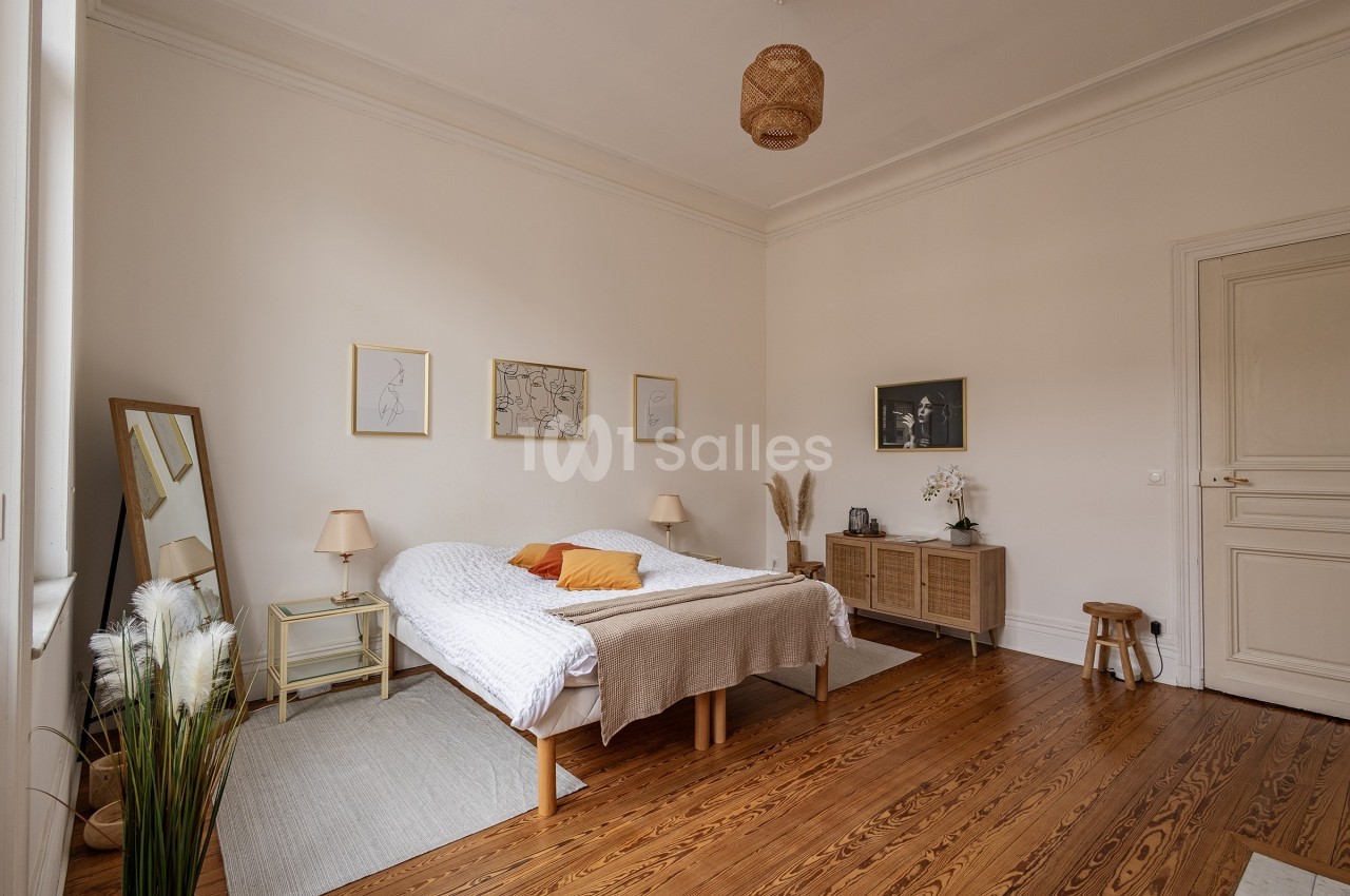 Chambre lumineuse avec lit double, parquet en bois, meubles en rotin, décor minimaliste et cadre épuré.
