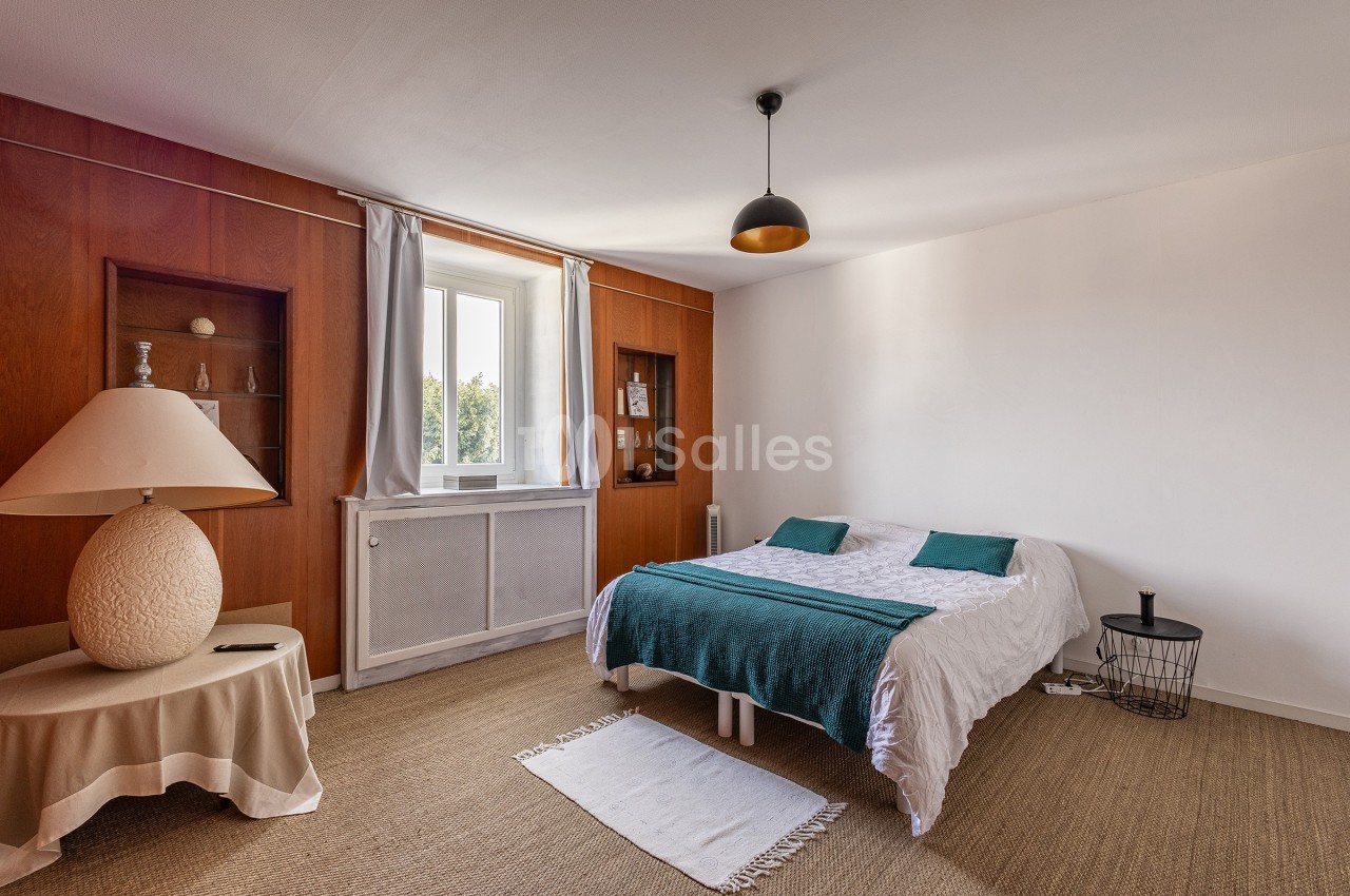 Chambre lumineuse avec lit double, décoration sobre, murs en bois et fenêtre donnant sur l'extérieur.