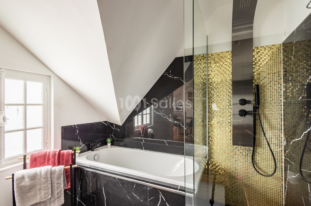Salle de bain avec baignoire encastrée, douche à l'italienne, carrelage noir marbré et mosaïque dorée.