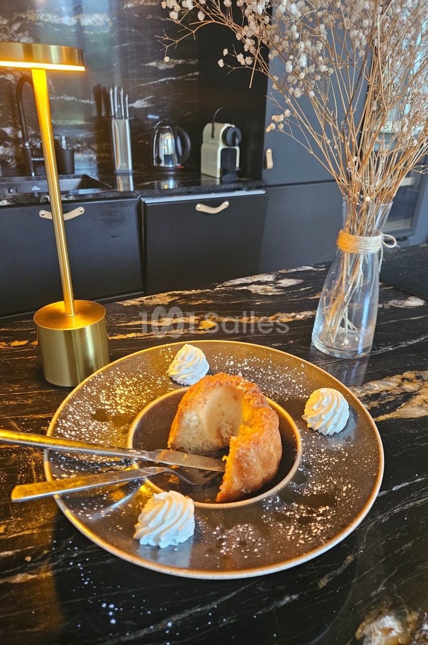 Dessert individuel avec crème chantilly sur une assiette, posé sur un plan de travail sombre avec une lampe et un vase.