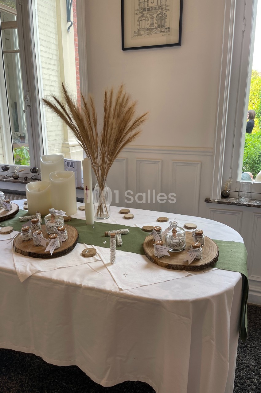 Table décorée avec des bougies, des herbes séchées et des petits pots en verre sur des rondins de bois, près d'une fenêtre.