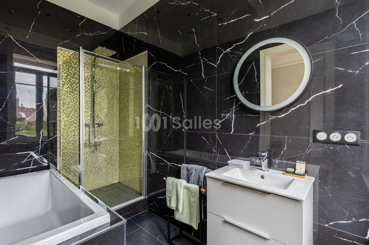 Salle de bain moderne avec murs en marbre noir, douche à mosaïque dorée, baignoire blanche et meuble vasque.