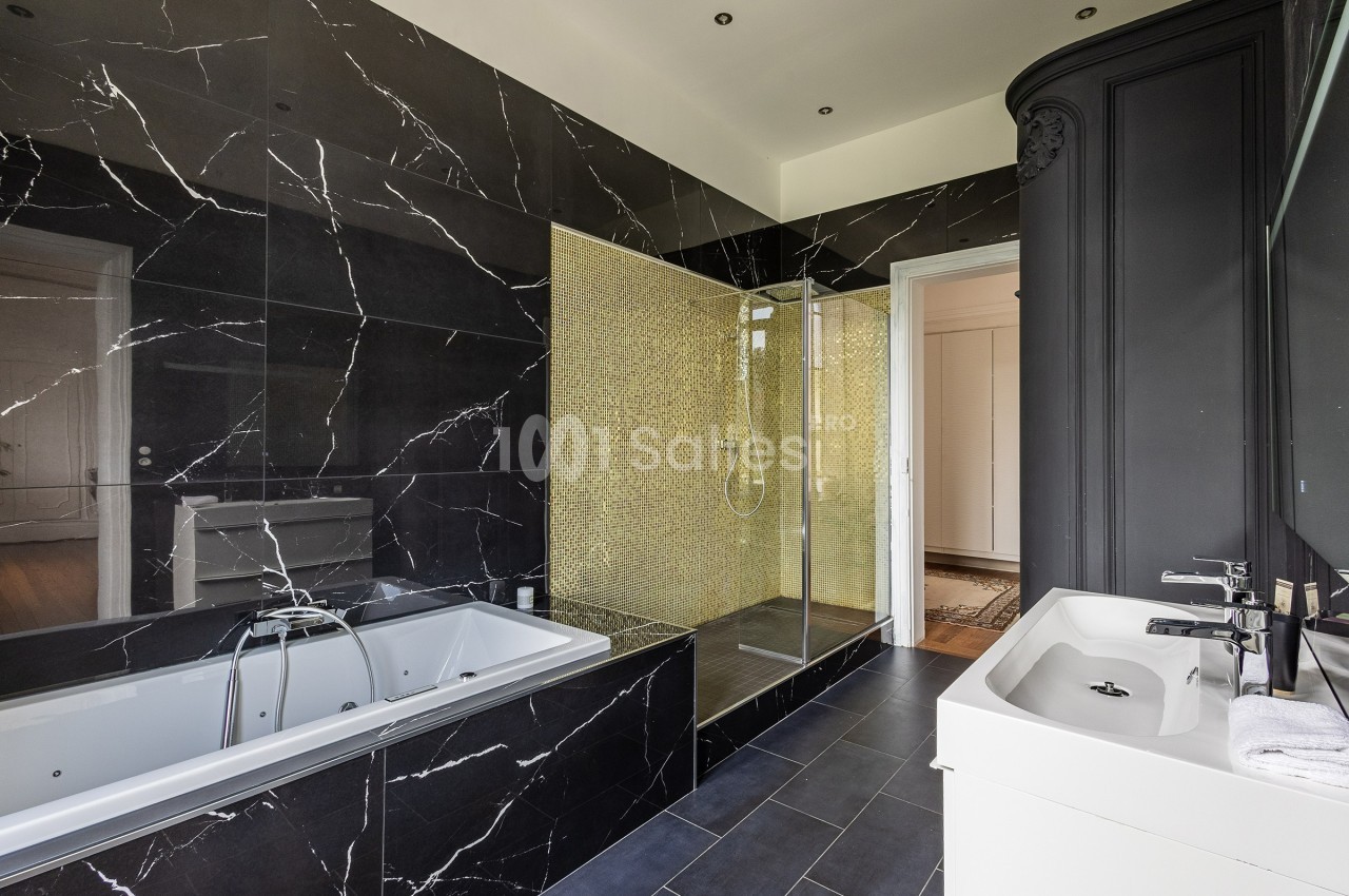 Salle de bain moderne avec baignoire encastrée, douche à l'italienne dorée et murs en marbre noir.