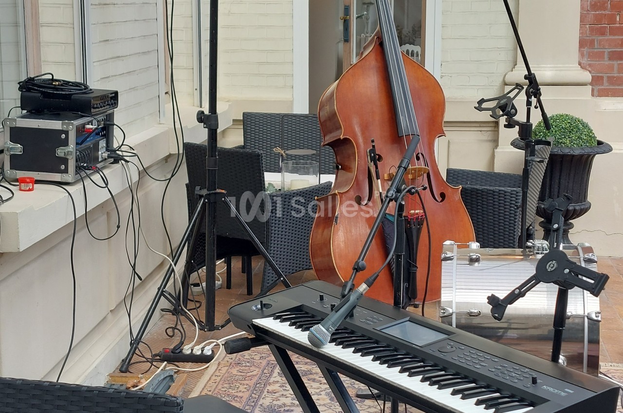 Clavier, contrebasse et matériel audio installés en extérieur sur une terrasse, prêts pour une performance musicale.