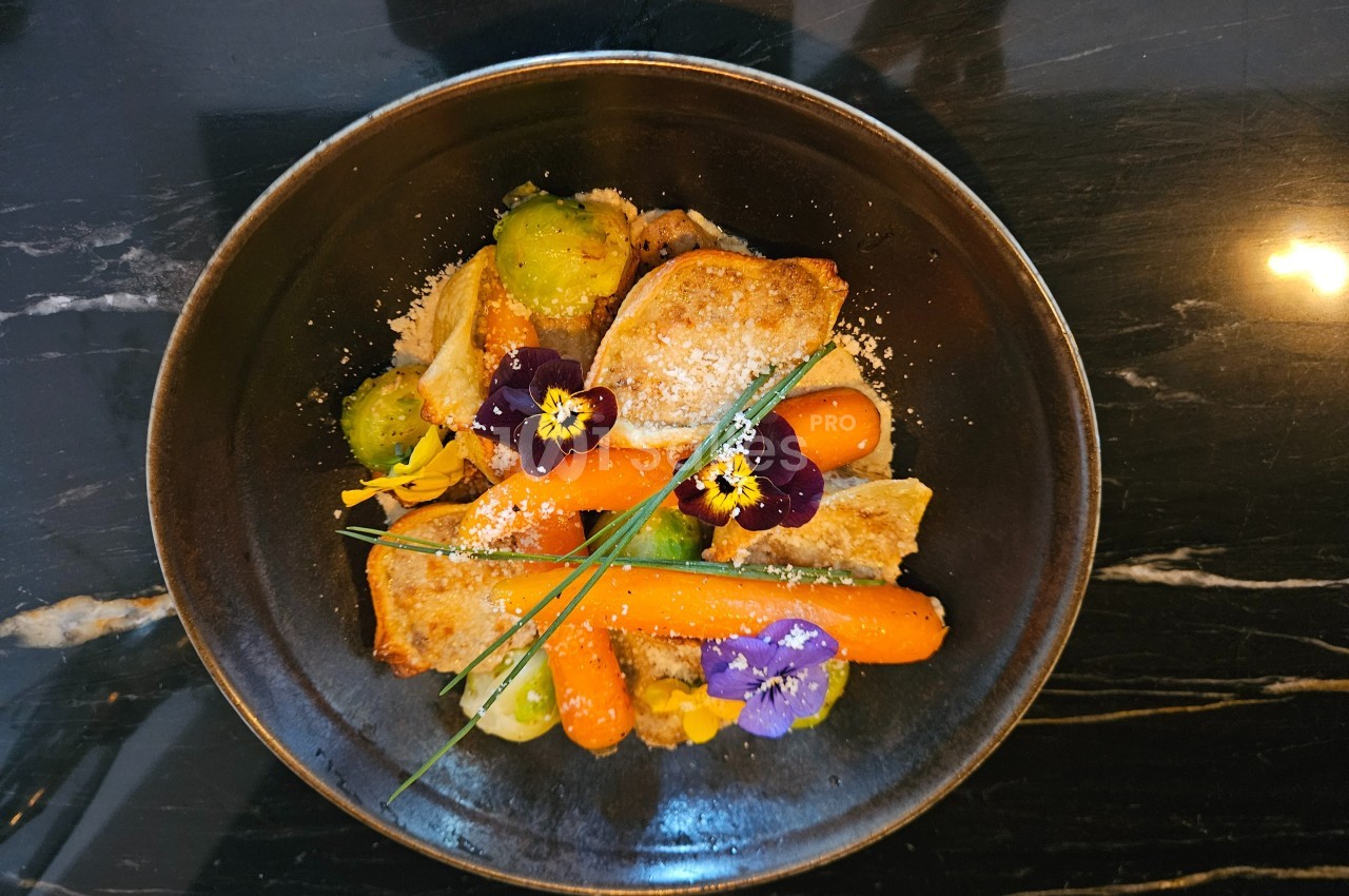 Assiette garnie de légumes colorés, fleurs comestibles et morceaux de viande, présentée sur une table en marbre noir.