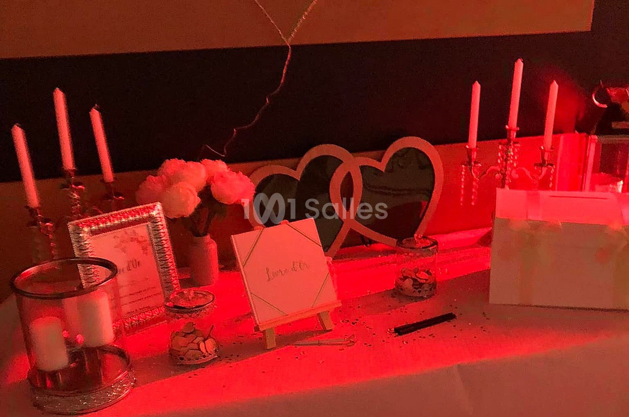 Table décorée avec des bougies, cadres, fleurs et une boîte blanche, éclairée par une lumière rouge tamisée.