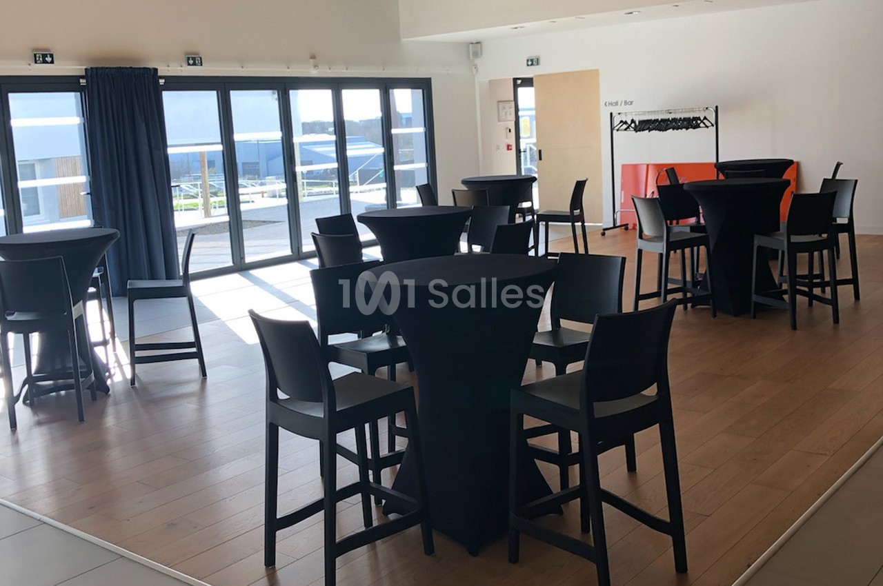 Salle lumineuse avec tables hautes noires, chaises assorties et une baie vitrée donnant sur une terrasse extérieure.