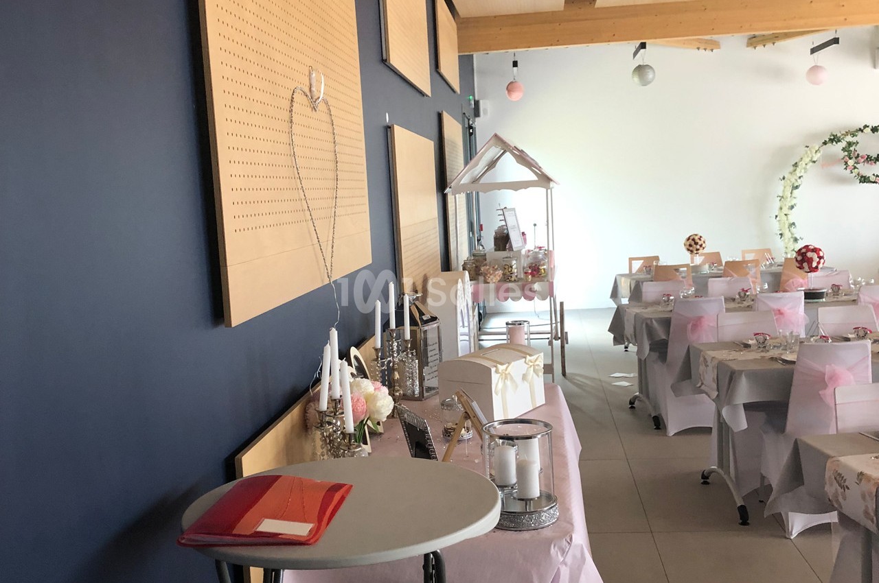 Salle décorée pour un événement avec tables habillées de nappes roses, décorations florales et coin buffet.