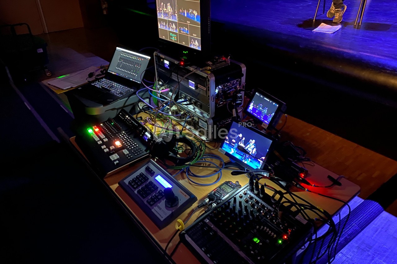 Poste de régie audiovisuelle avec consoles, écrans et câblages, utilisé pour gérer une production en direct sur scène.