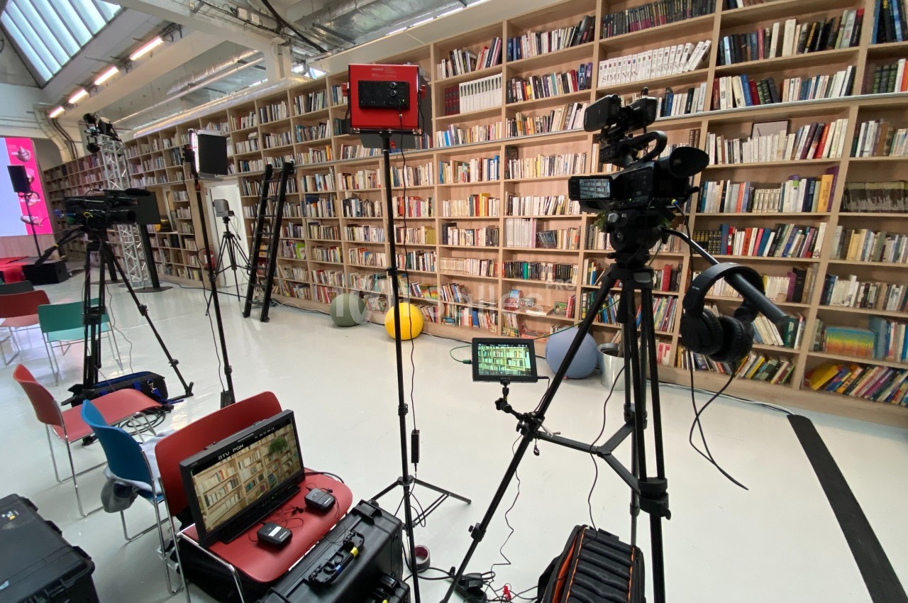 Équipement de tournage installé dans une bibliothèque avec des caméras, trépieds et éclairages.