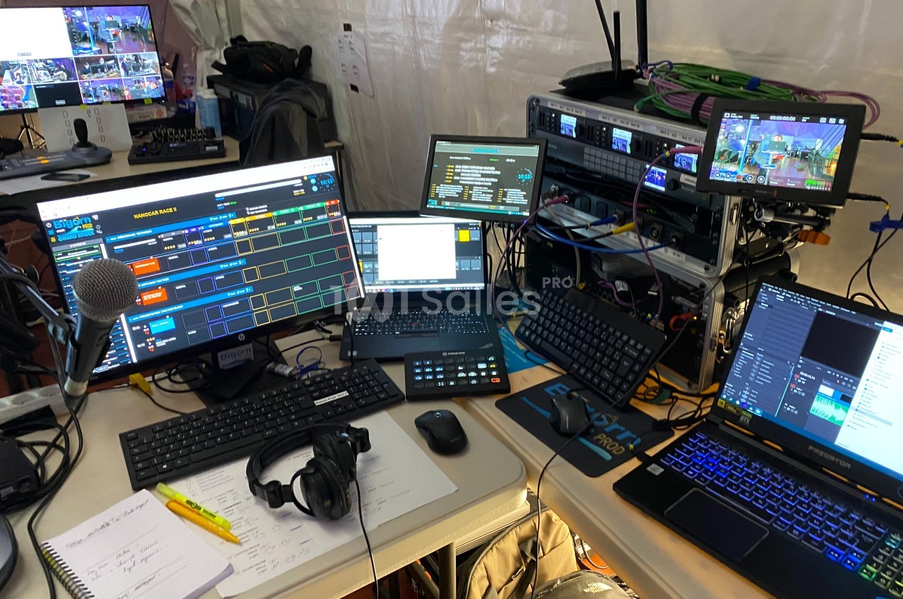 Poste de travail technique avec plusieurs écrans, ordinateurs, équipements audio et notes manuscrites.