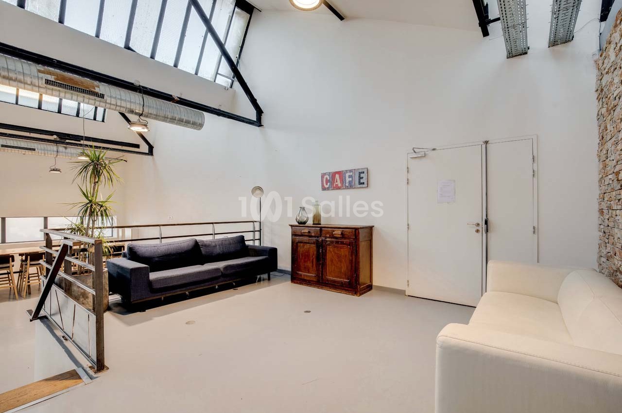 Espace lumineux avec canapé, fauteuil, meuble en bois et mur en briques, sous une verrière inclinée.