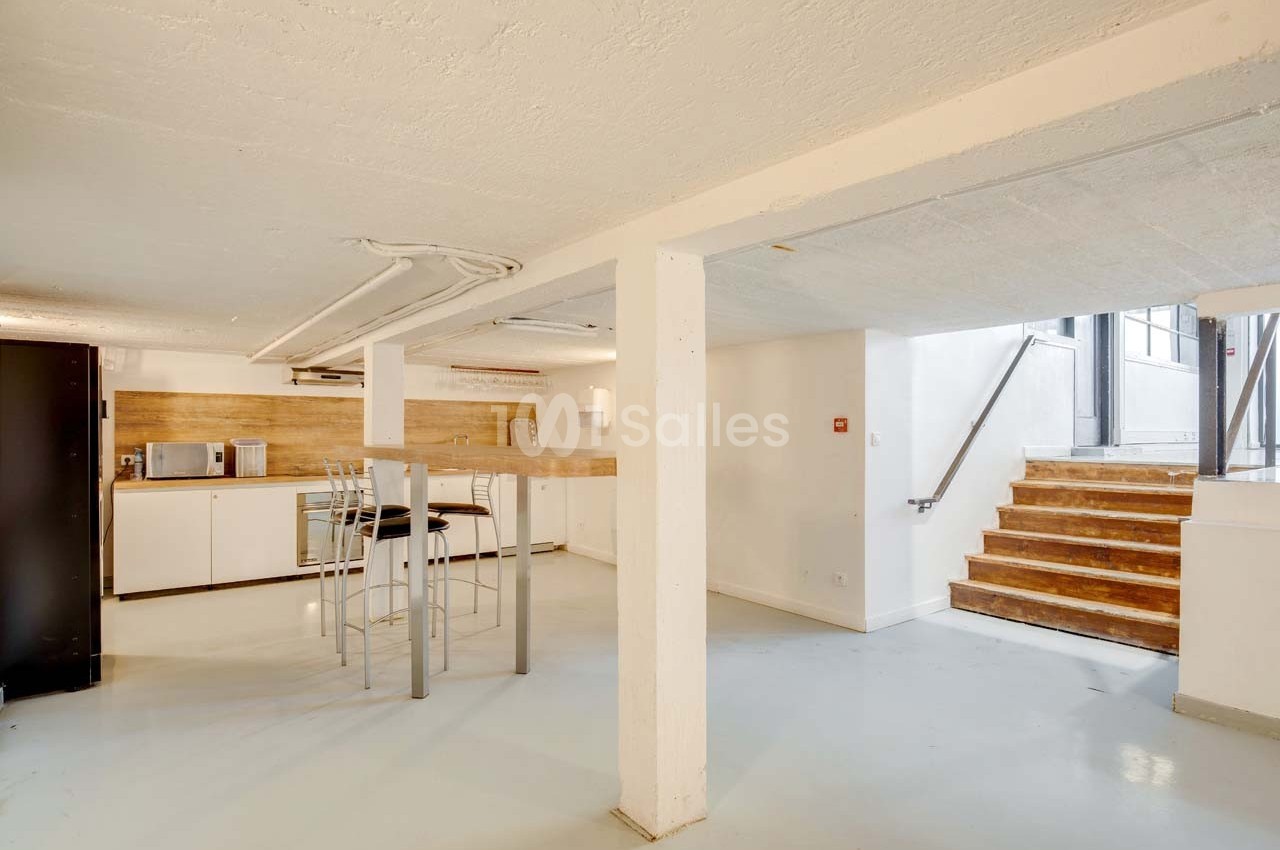 Cuisine ouverte avec comptoir en bois, tabourets hauts, électroménager moderne et escalier menant à une porte vitrée.