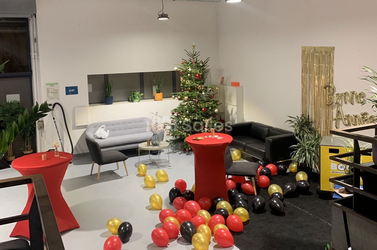 Salle décorée pour une fête avec ballons rouges, noirs et dorés, sapin de Noël et pancarte ’Bonne Année’.