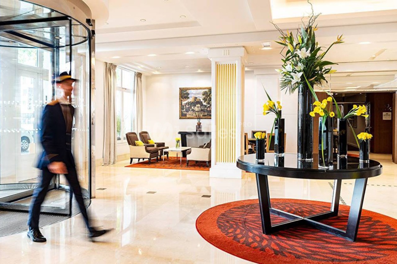 Hall d'entrée lumineux avec un tapis rouge, une table décorée de fleurs et un portier en mouvement.