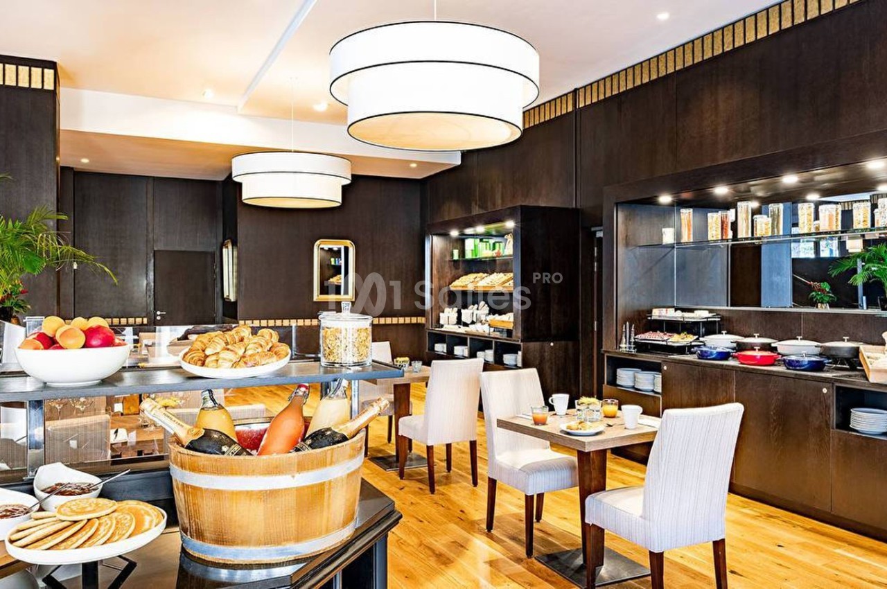 Salle de petit-déjeuner avec buffet varié, tables dressées, éclairage chaleureux et décor moderne en bois sombre.