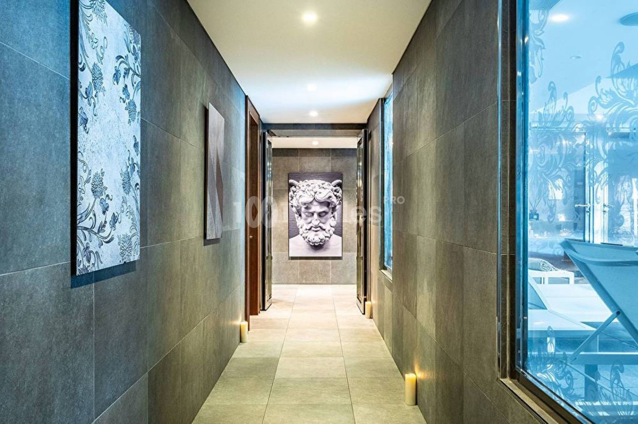 Couloir moderne avec murs en carrelage sombre, tableaux décoratifs et lumière douce, donnant sur une salle vitrée.