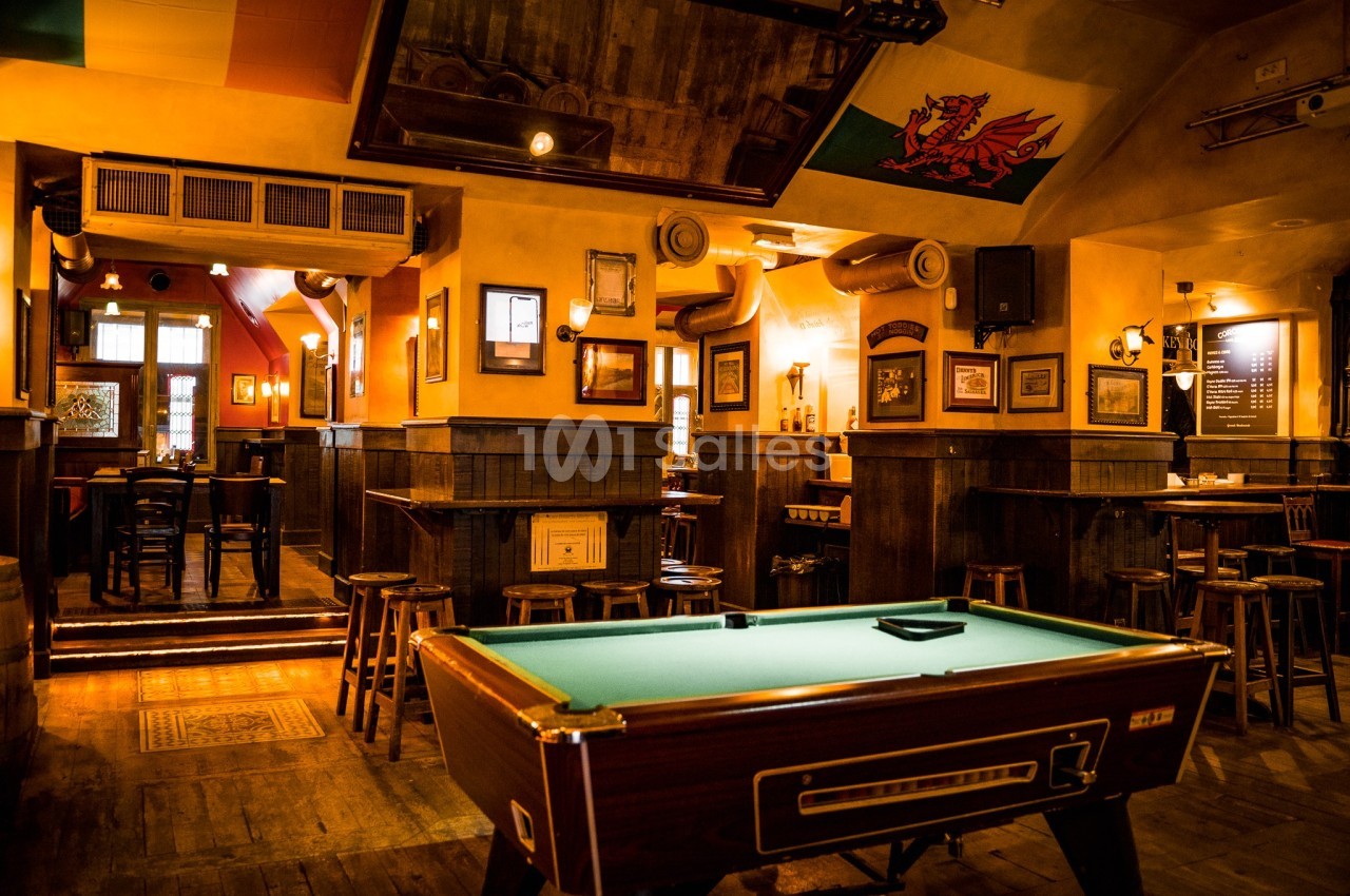 Salle de pub chaleureuse avec un billard au premier plan, des tables en bois et des décorations murales.
