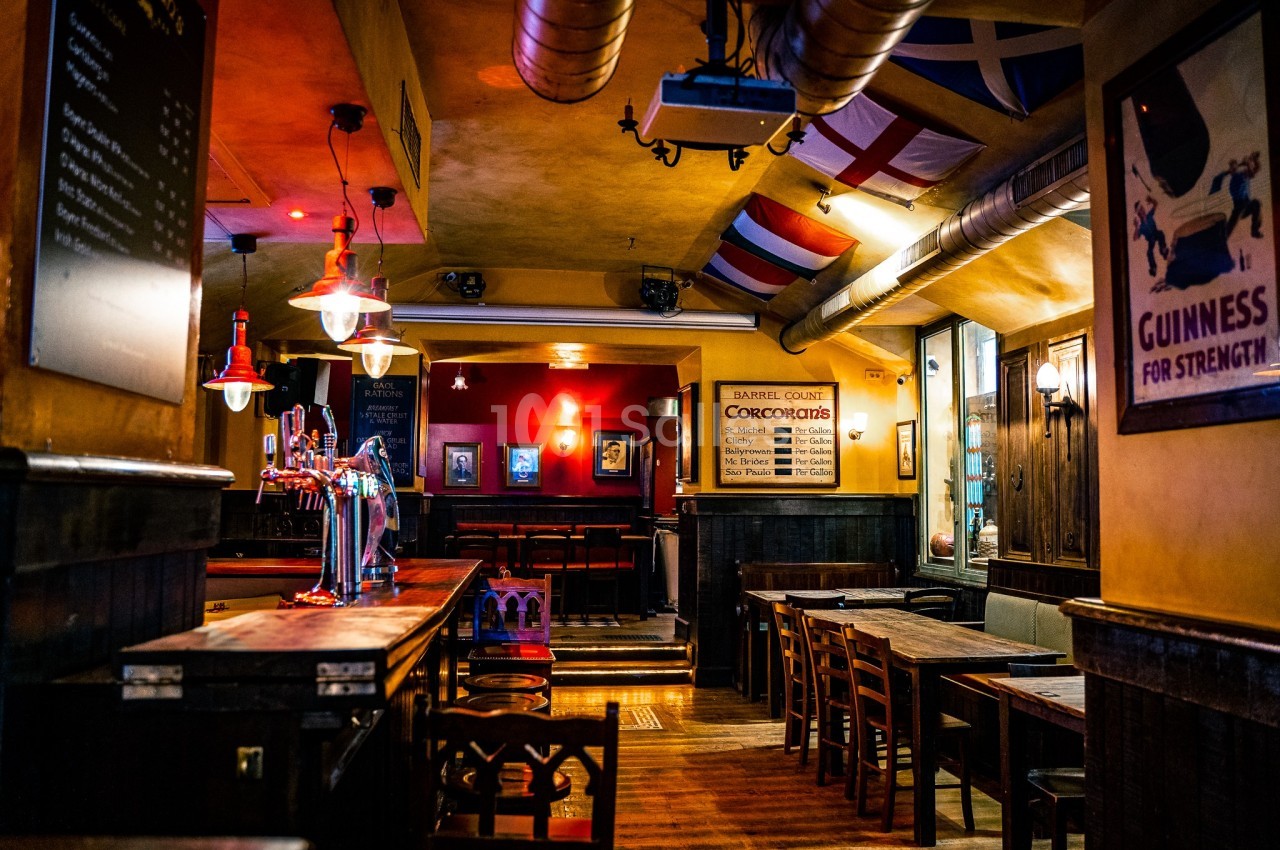 Intérieur d'un pub chaleureux avec tables en bois, bar équipé de tireuses et drapeaux suspendus au plafond.