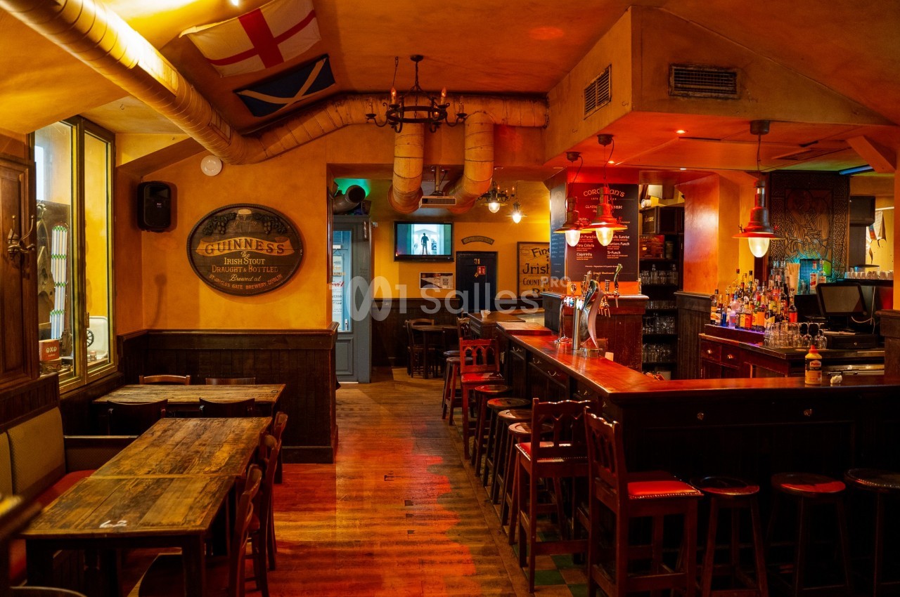 Intérieur d'un pub chaleureux avec bar en bois, tables, chaises et décorations murales aux tons chauds.