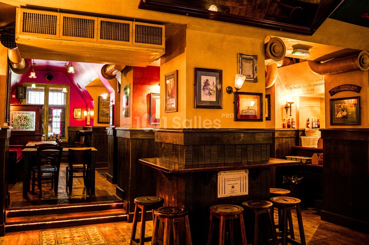 Intérieur d'un bar chaleureux avec des tables en bois, des tabourets et une lumière tamisée.