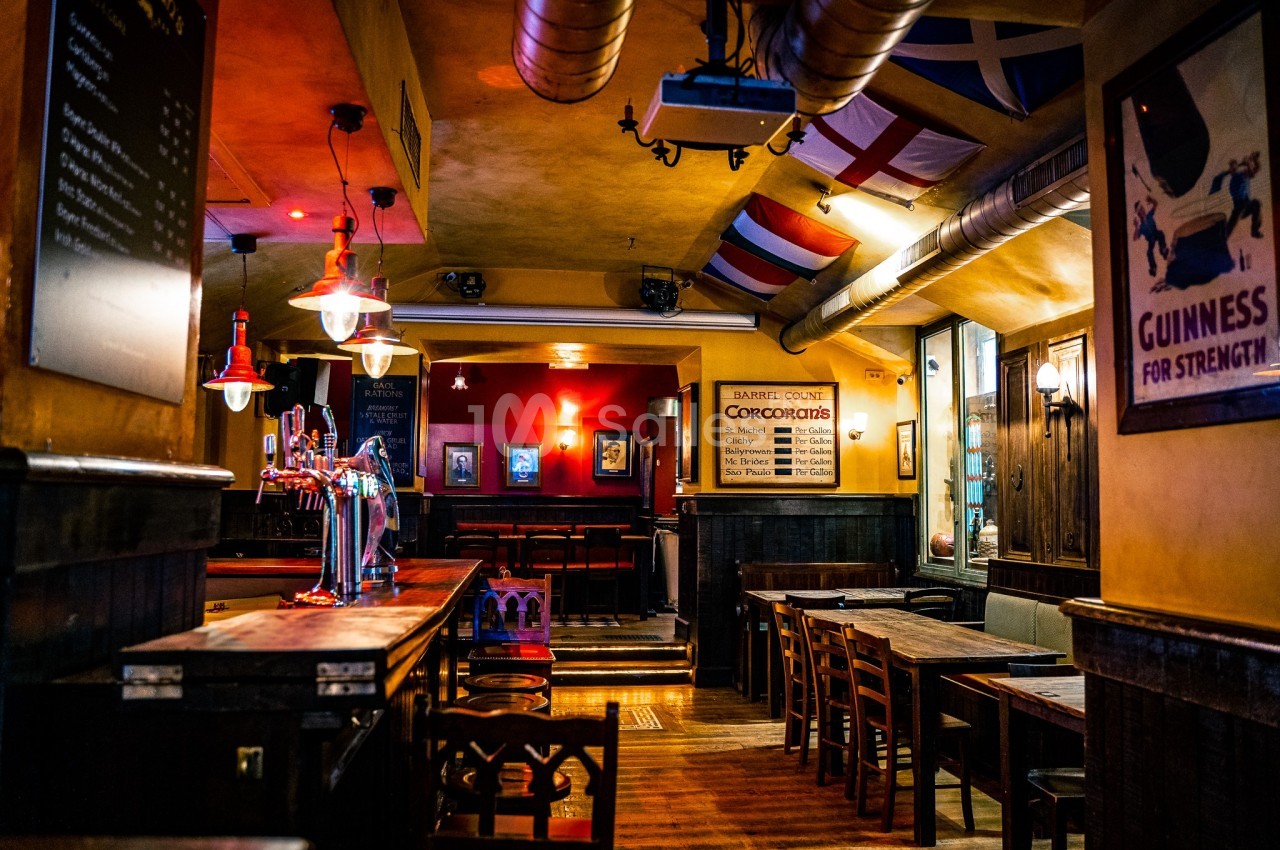 Intérieur d'un pub chaleureux avec des tables en bois, un bar éclairé et des drapeaux suspendus au plafond.