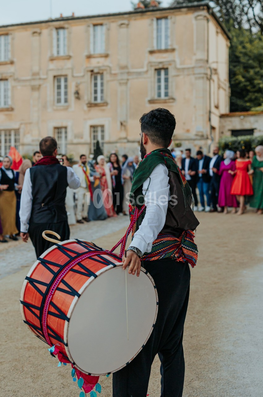 Un musicien joue du tambour devant un groupe de personnes rassemblées près d'un bâtiment ancien.