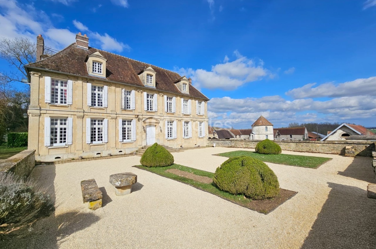 Façade d'une maison de style classique avec jardin aménagé, ciel bleu et quelques nuages en arrière-plan.