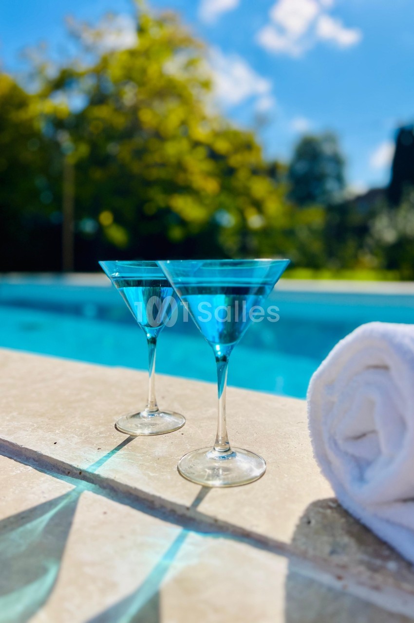 Deux verres de cocktail bleu posés sur le bord d'une piscine, avec une serviette blanche enroulée à côté.