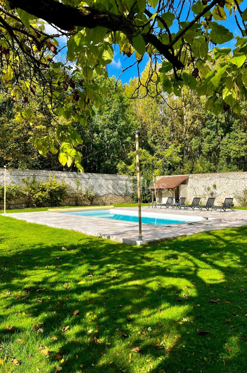 Piscine extérieure entourée de verdure, avec des transats alignés sur une terrasse en pierre et un mur en arrière-plan.