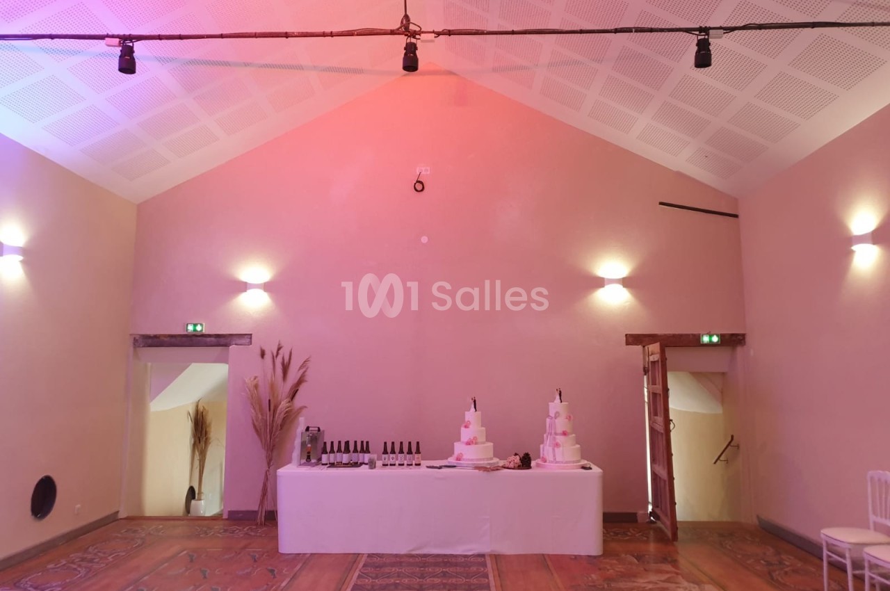 Table décorée avec des bouteilles de vin et un gâteau de mariage à plusieurs étages dans une salle aux murs beige clair.