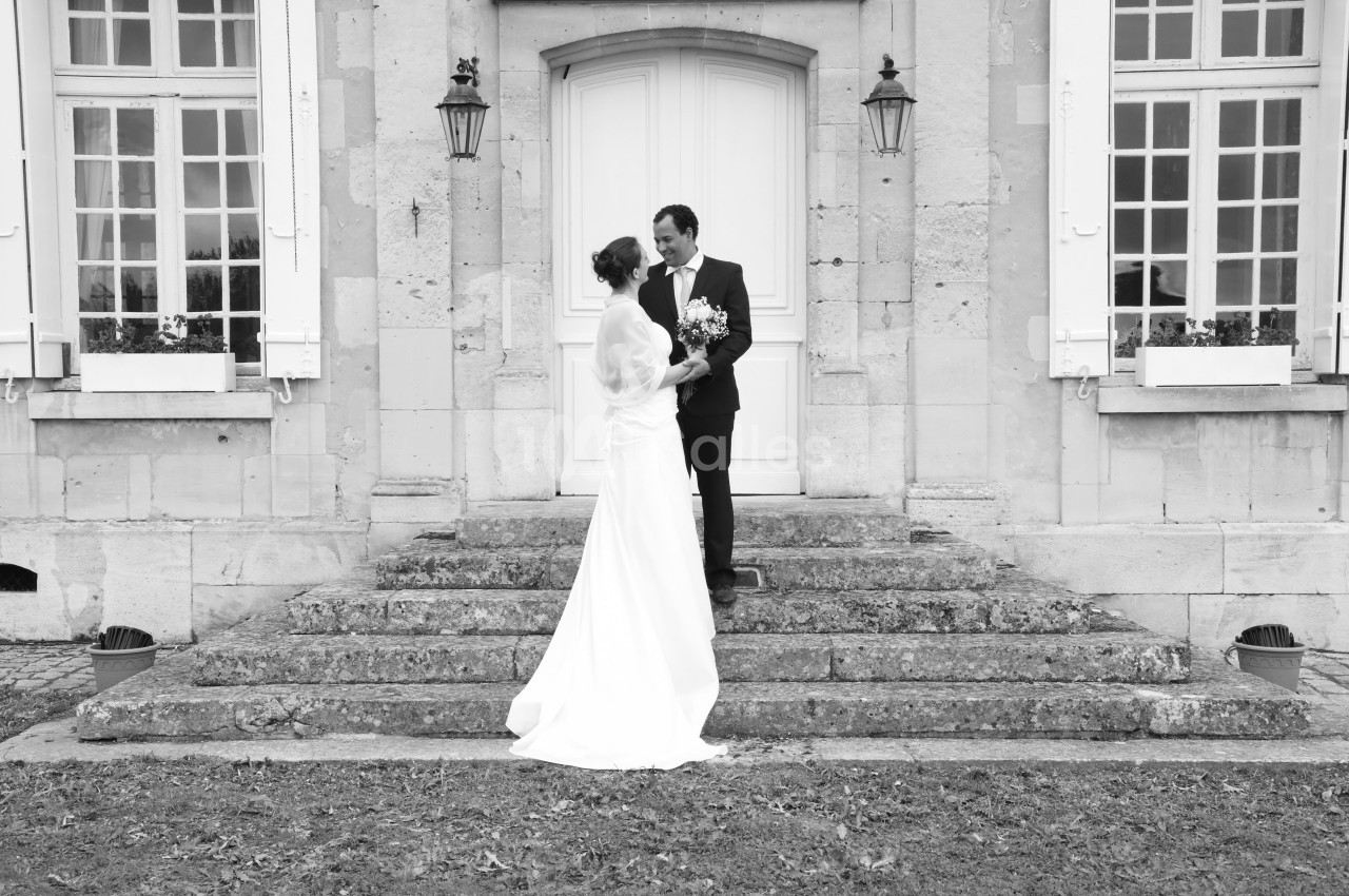Un couple en tenue de mariage pose sur les marches devant une porte d'entrée d'un bâtiment en pierre.