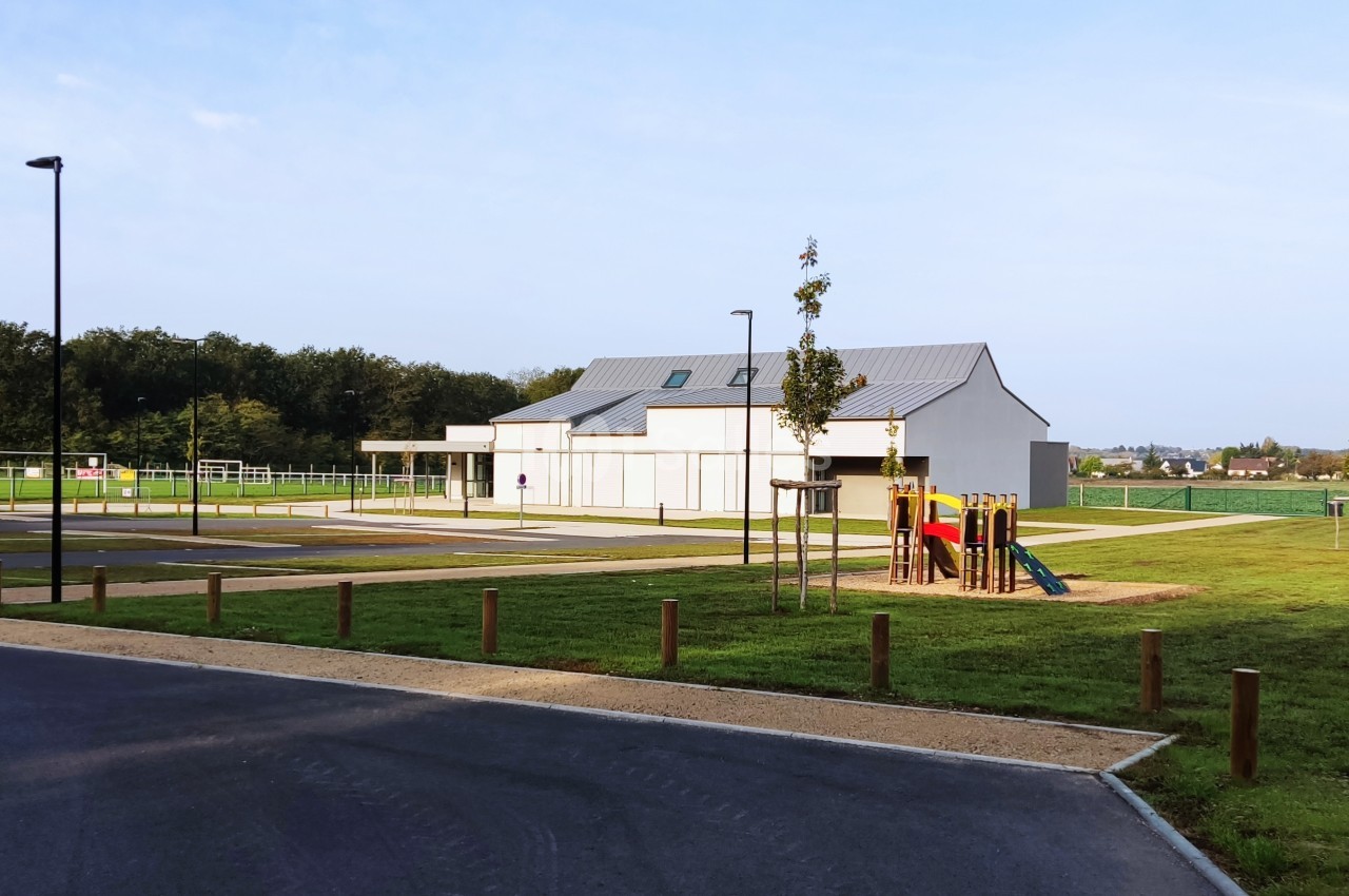 Bâtiment moderne entouré d'espaces verts, avec une aire de jeux pour enfants et un parking à proximité.