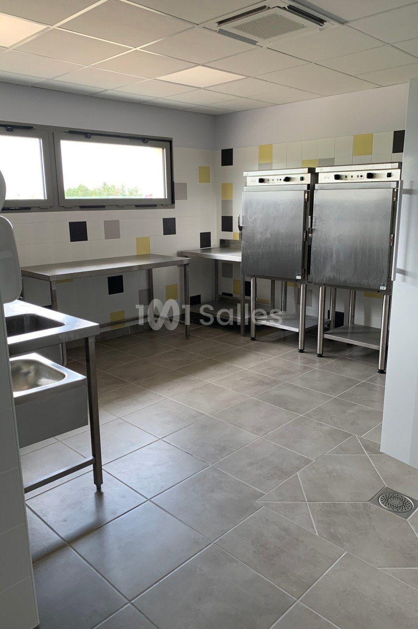 Cuisine professionnelle avec éviers en inox, plans de travail, carrelage au sol et murs ornés de carreaux colorés.
