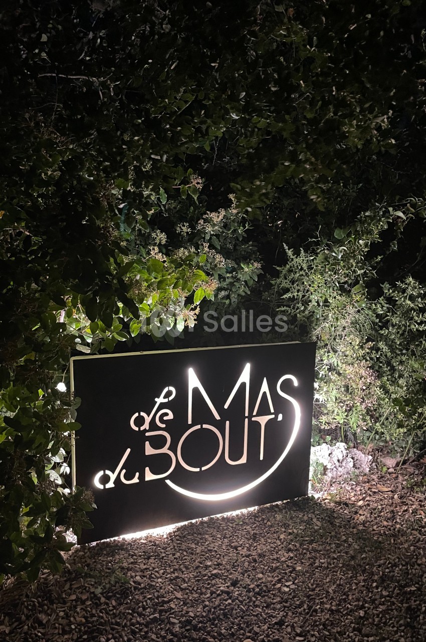Panneau lumineux ’Le Mas du Bout’ entouré de végétation, photographié de nuit.