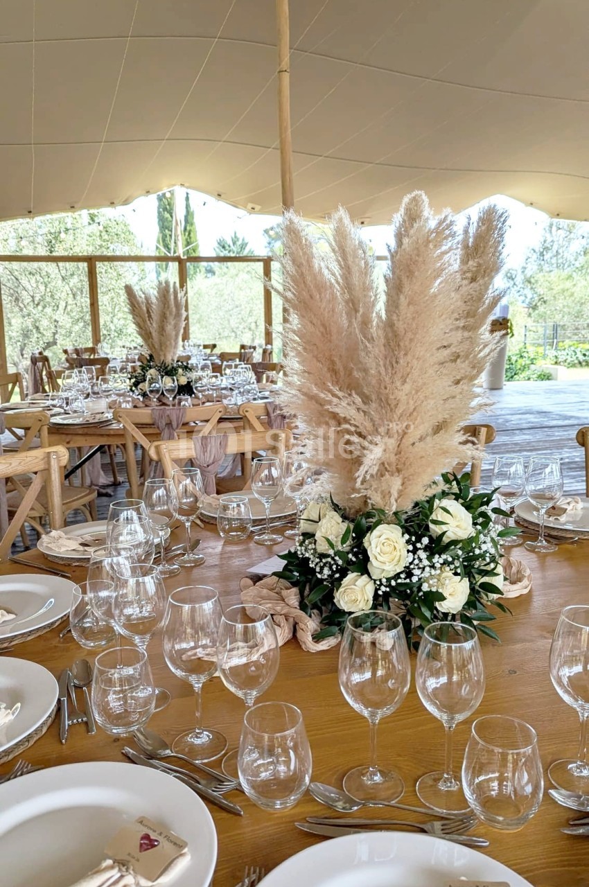 Table de réception décorée avec des roses blanches, des herbes de la pampa et une vaisselle élégante sous une tente ouverte.