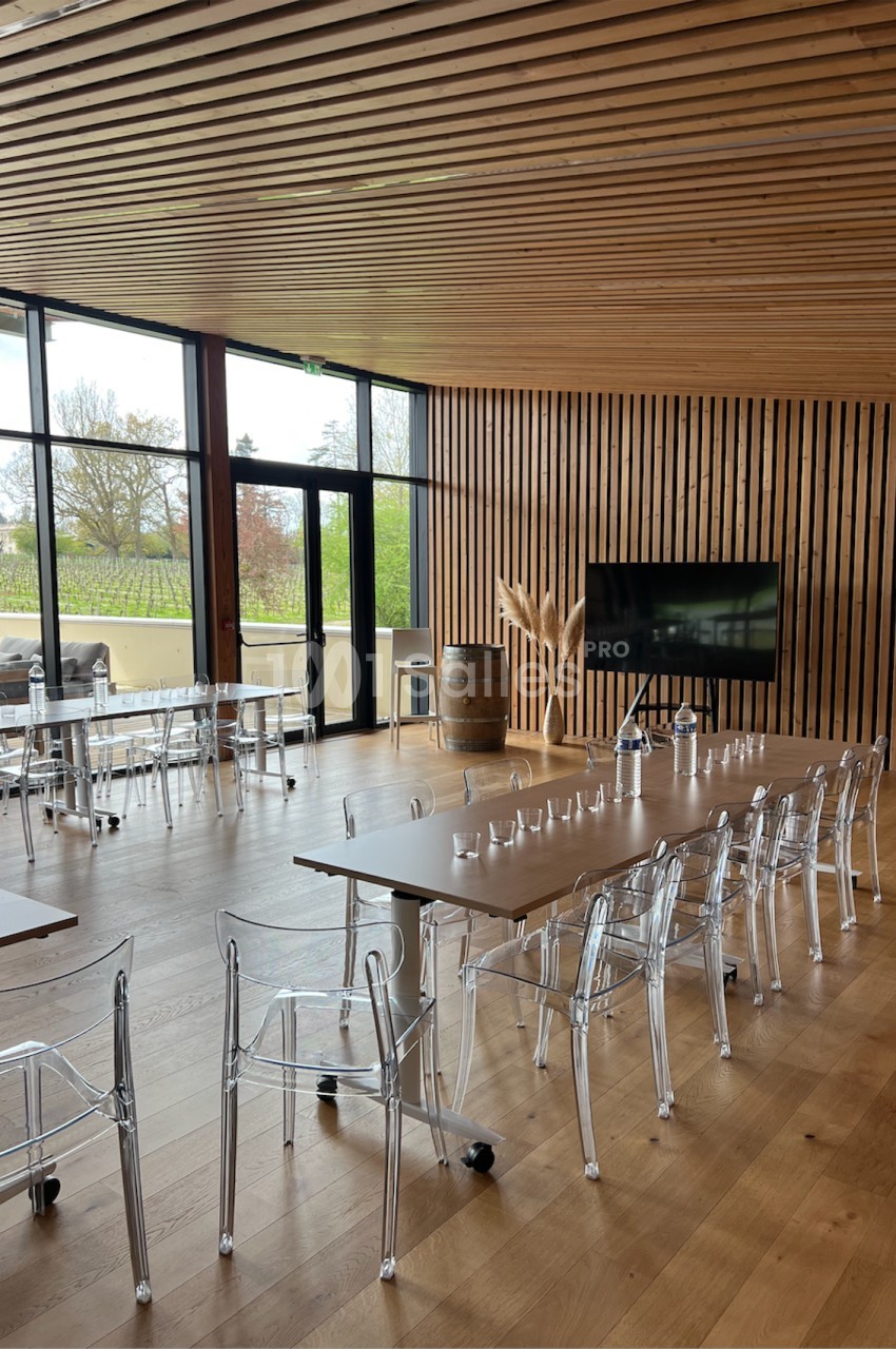 Salle de réunion lumineuse avec tables en bois, chaises transparentes, écran et grandes baies vitrées donnant sur l…