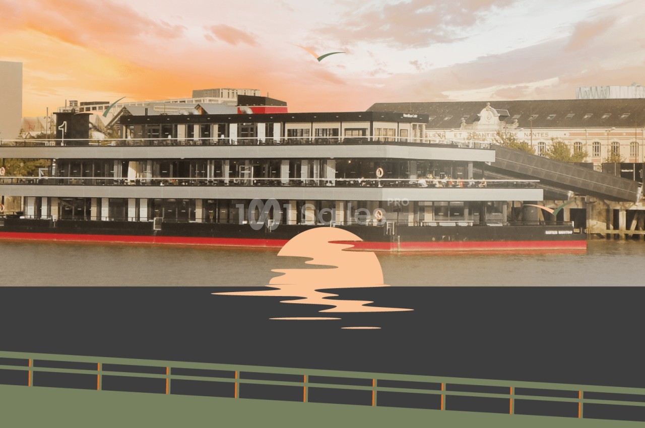 Bateau moderne à plusieurs étages amarré sur une rivière au coucher du soleil, avec un bâtiment en arrière-plan.
