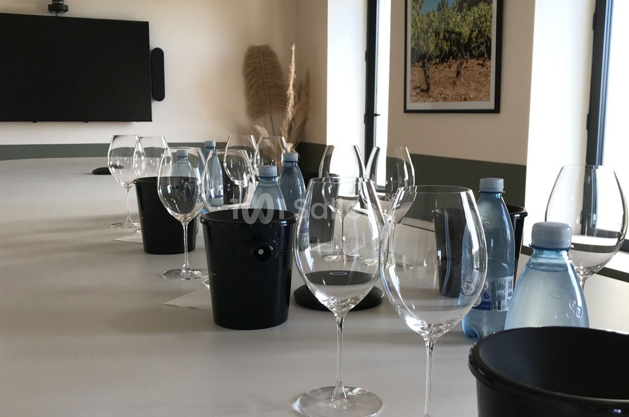 Table dressée avec des verres à vin, seaux noirs et bouteilles d'eau dans une salle lumineuse décorée sobrement.