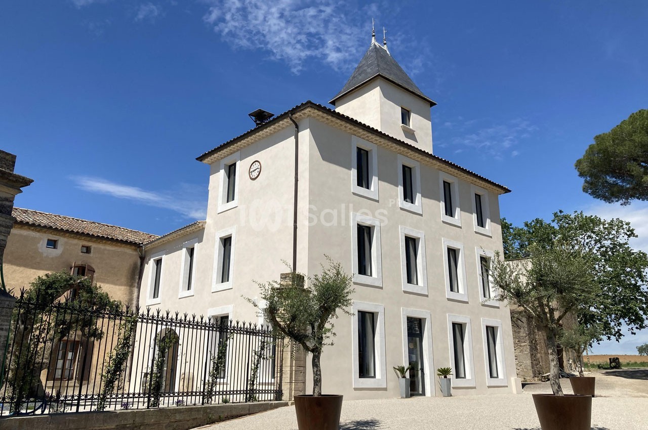 Façade d'un bâtiment rénové de style traditionnel, entouré d'arbres et de pots décoratifs sous un ciel dégagé.