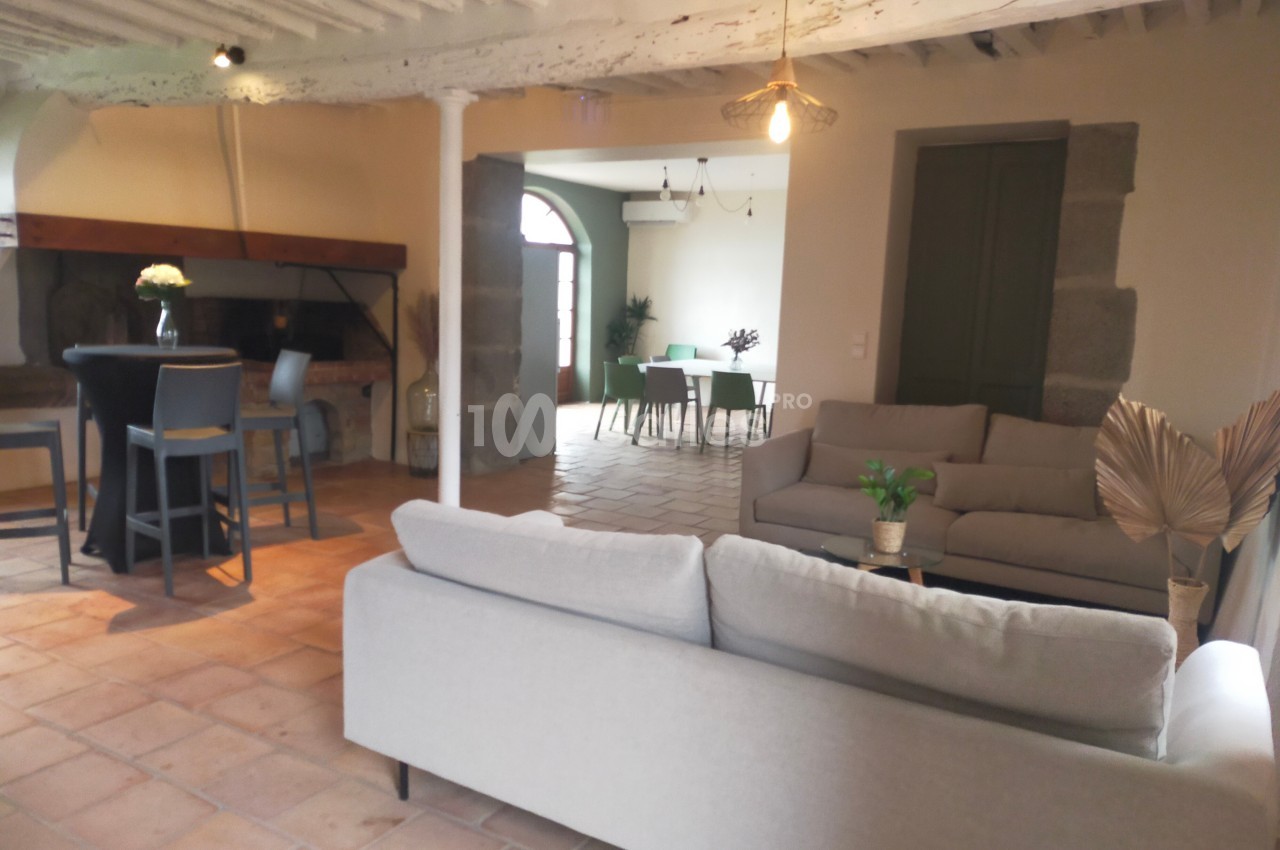 Salon lumineux avec canapés gris, table haute près d'une cheminée et vue sur une salle à manger en arrière-plan.