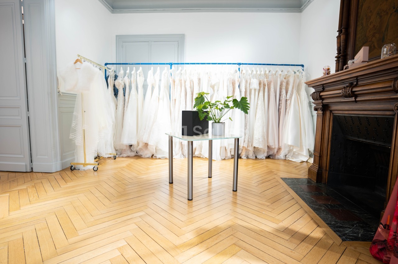 Portant de robes blanches élégantes dans une pièce lumineuse avec parquet, table en verre et cheminée en bois.