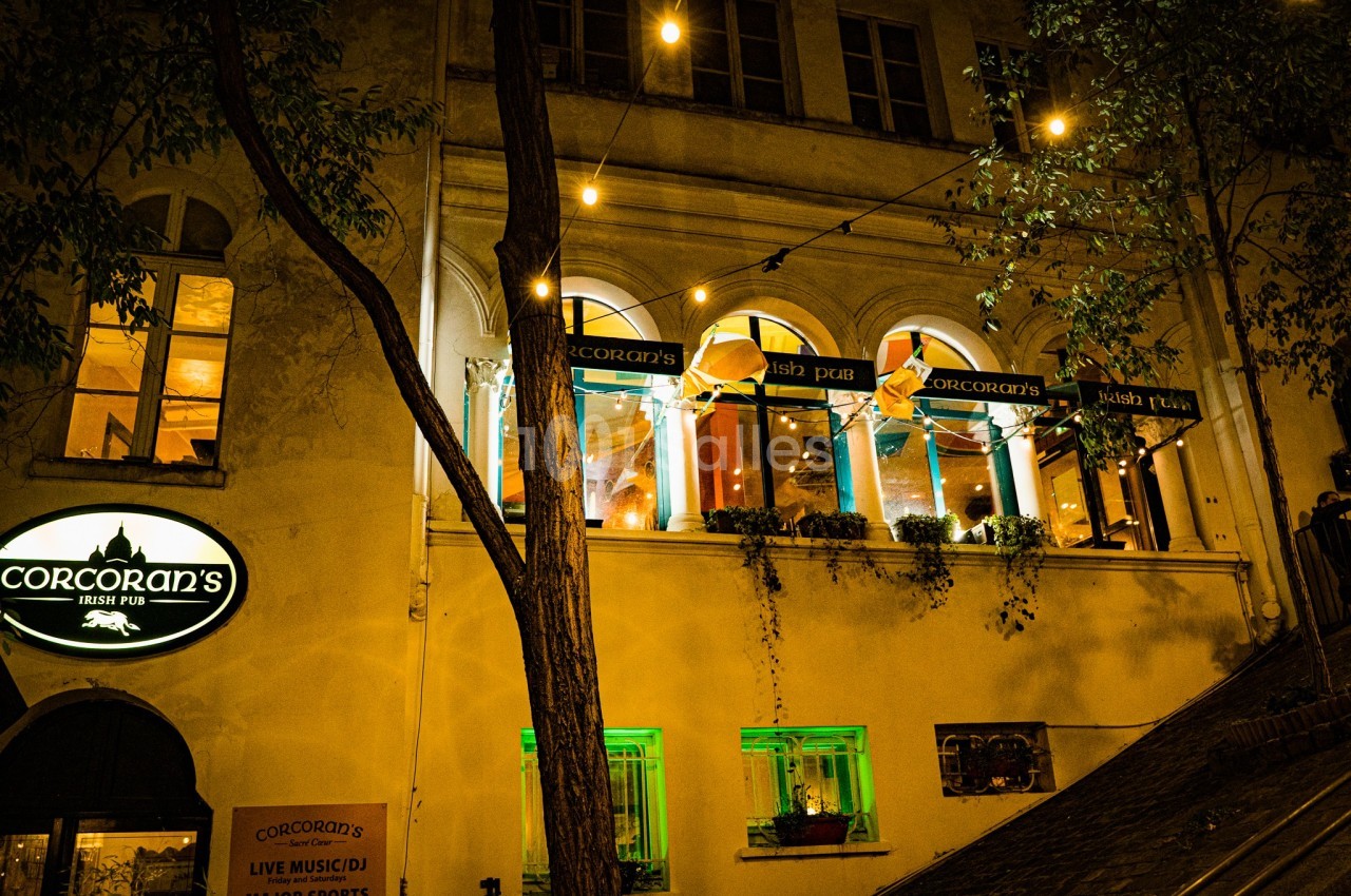 Façade d'un pub irlandais éclairé la nuit, avec des guirlandes lumineuses et des fenêtres décorées.